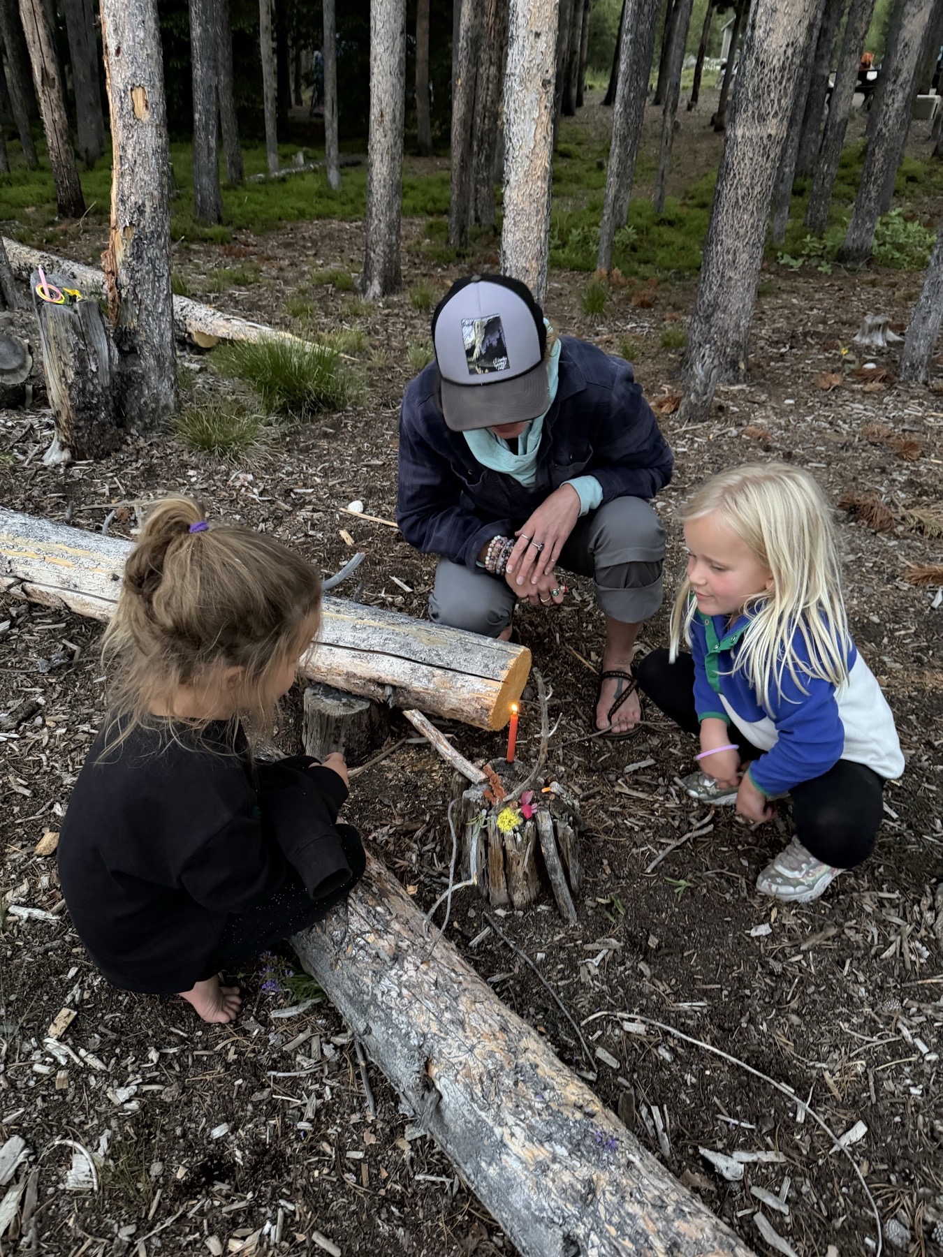 Chasta and children gathered around a small candle and forest ritual